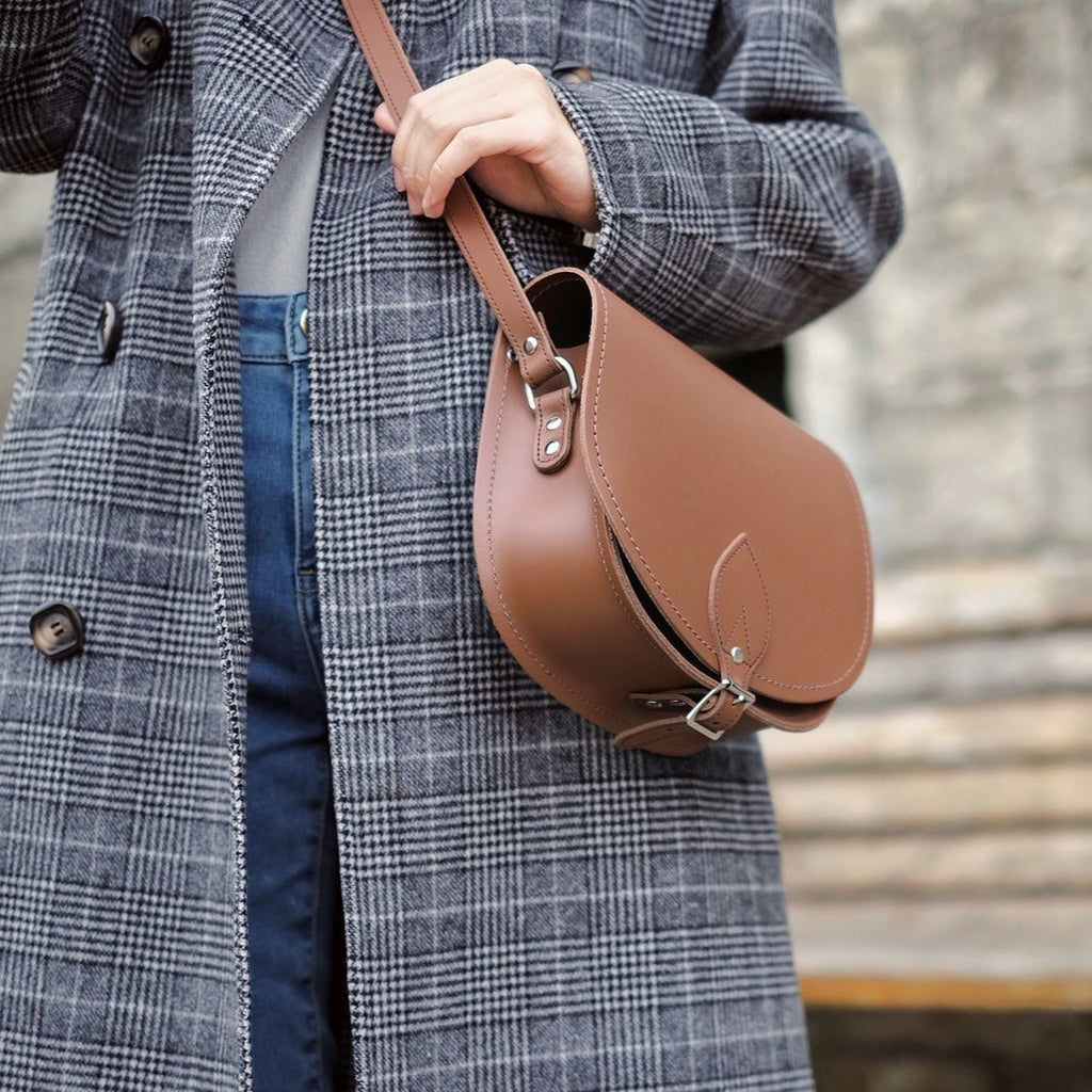 Person wearing a plaid coat holding a brown leather bag.