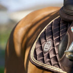Close-up of a horse saddle with a brown leather cover and quilted design, featuring the 'HALT' brand logo.