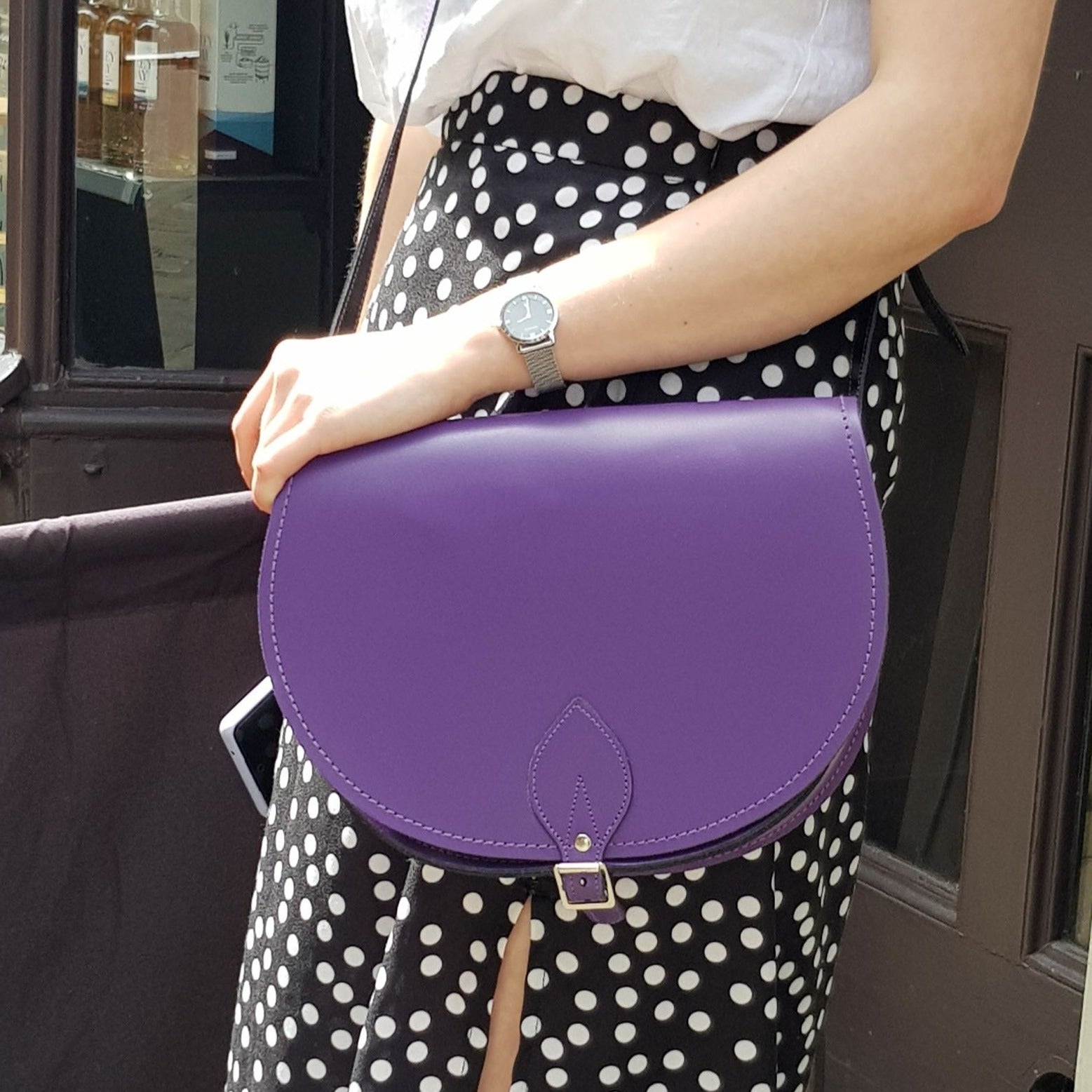 Person holding a purple handbag with a polka dot skirt and watch.