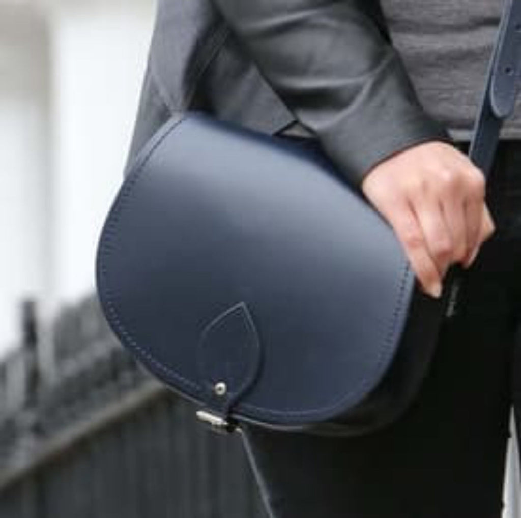 Person holding a navy blue saddle-shaped bag with a blurred background