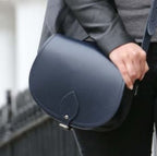 Person holding a navy blue saddle-shaped bag with a blurred background