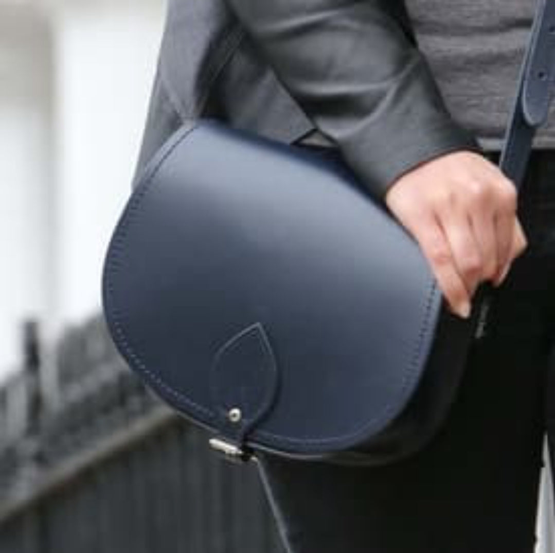 Person holding a navy blue saddle-shaped bag with a blurred background